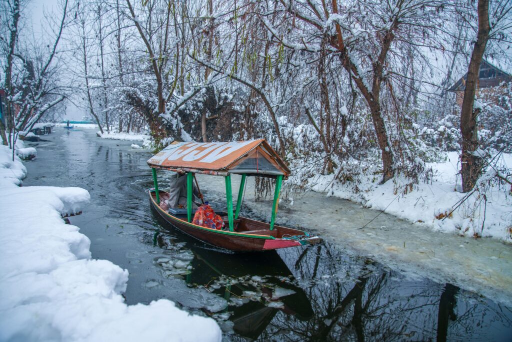 A tranquil scene of a wooden boat on a snowy canal in Kashmir, India.